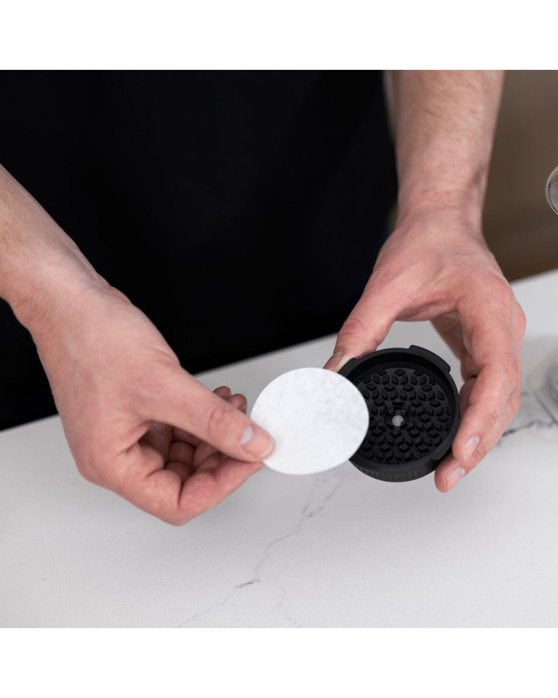 Manos colocando un filtro de papel AeroPress dentro de la tapa Flow Control