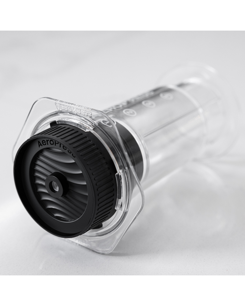 Tapa Flow Control enroscada en una AeroPress Clear apoyada sobre encimera de mármol