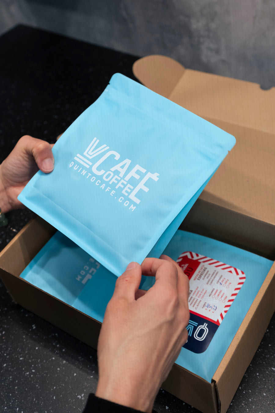 Hands opening a Quinto Café shipping box with the bag of coffee