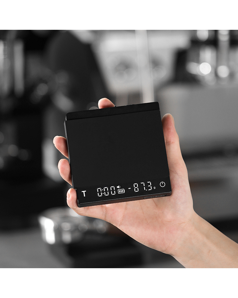 Mano sujetando la báscula Cube 2.0 Mini encendida con temporizador y peso en pantalla