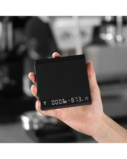 Mano sujetando la báscula Cube 2.0 Mini encendida con temporizador y peso en pantalla